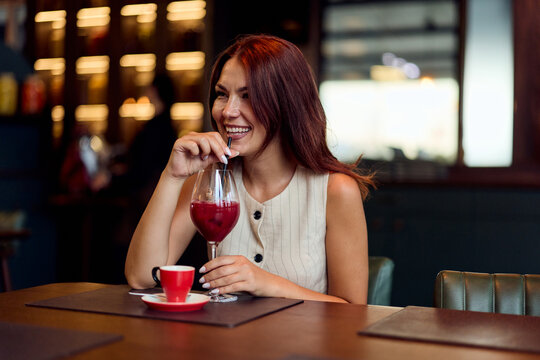 Smiling Young Woman Drinking Red Cocktail In Modern Cafe During Casual Brunch And Social Outing