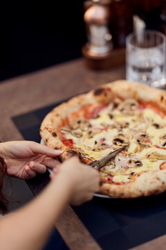 Person Cutting A Mushroom Pizza at a Restaurant Table During Casual Lunch or Dinner With Friends