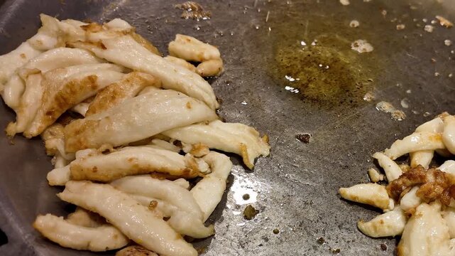 Close-up of seafood pieces frying on a large flat griddle at a Thai food market, showing an authentic street food cooking process.