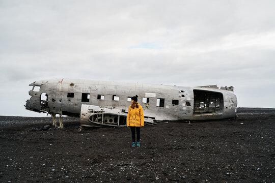 A white woman stands by crashed airplane wreckage on volcanic terrain