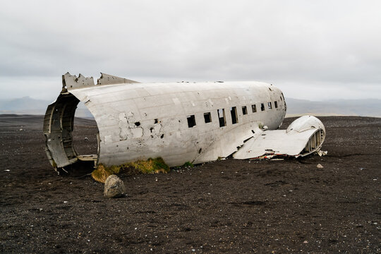 A wrecked airplane fuselage lies abandoned on black sand