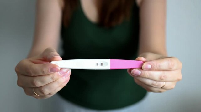 Selective focus of a woman's hands reaching out and showing a positive pregnancy test kit.