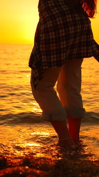 Golden sunset illumination outlines a girl standing amidst ocean surf on the beach as she moves rhythmically. Static low-angle shot.