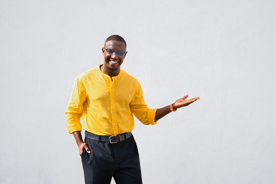 Gesturing with open palm at copy space, african american man, businessman consultant has friendly, smiling expression in casual isolated studio business portrait. Young professional presenting new