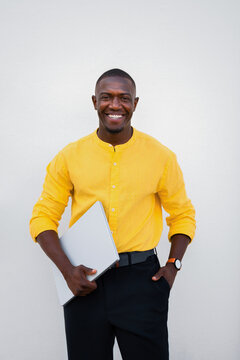 African american man, businessman carrying laptop, vertical casual isolated studio business portrait, proud and smiling expression. Young banker holds modern computer technology device confidently for