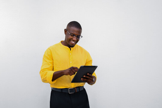 Looking down, african american man, businessman reviews data on tablet, focused and smiling expression in casual isolated studio business portrait with copy space. Young accountant browsing financial
