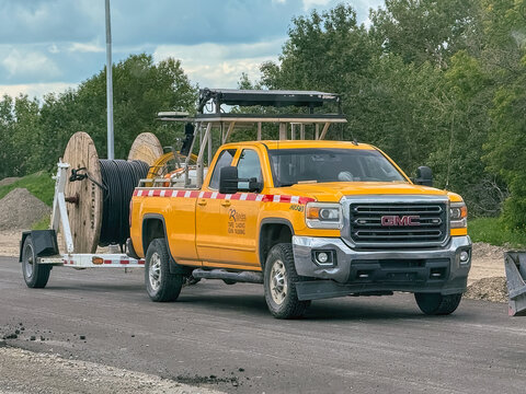 Calgary, Alberta, Canada. August 17, 2026. Front side view of a yellow GMC utility truck towing a trailer with a large cable spool.