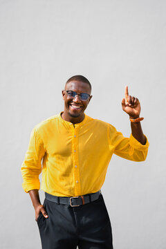 Pointing upward, african american man, businessman founder has cheerful, smiling expression in vertical casual isolated studio business portrait with copy space. Young professional presenting new idea