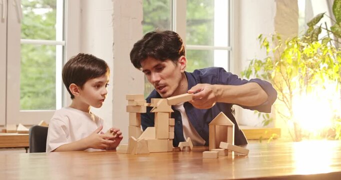 Father and young son building imaginative structures with wooden blocks together at home. Concept of educational toy ads, early learning content and parenting services.
