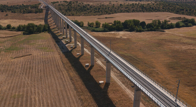 Portugal - 14 August 2026: Aerial view of a long railway viaduct stretching across a dry, rural landscape with golden fields and scattered trees under a clear sky.