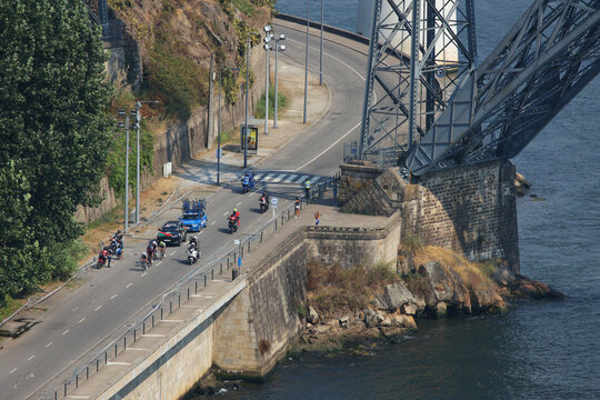 Porto, Portugal - 16 August 2026: View of a group of cyclists riding along the road beneath the stone structure of the Dom Luis I Bridge in Porto, Portugal.