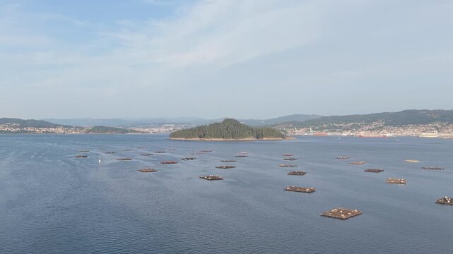Wide aerial shot of Illa de Tambo island surrounded by calm blue waters and numerous mussel farming platforms in the Ria de Pontevedra, near Combarro, Galicia, Spain.