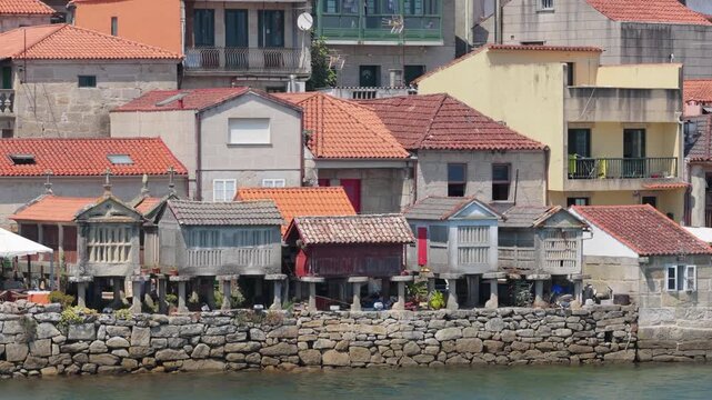 Static shot of traditional stone granaries, known as horreos, and old houses with red tiled roofs along the waterfront in Combarro, Galicia, Spain.