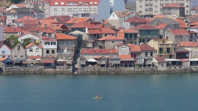 A wide shot of the waterfront in Combarro, Spain, featuring traditional stone houses with red-tiled roofs lining the shore.