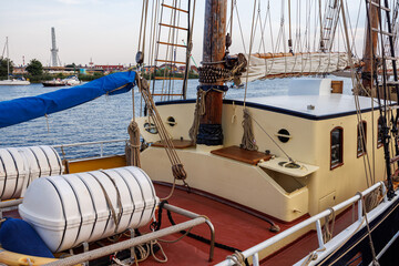 Wooden deck and cabin of a vintage sailing ship with white life rafts, ropes, and masts on a calm river. © Dmytro
