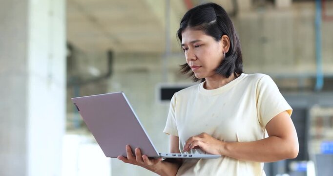 Asian woman using a laptop in a modern building, remote work, digital business, technology, communication, productivity, and professional lifestyle