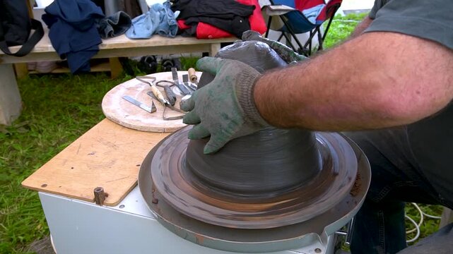  potter shapes a clay piece on a pottery wheel. Hands mold wet clay to create a ceramic object.