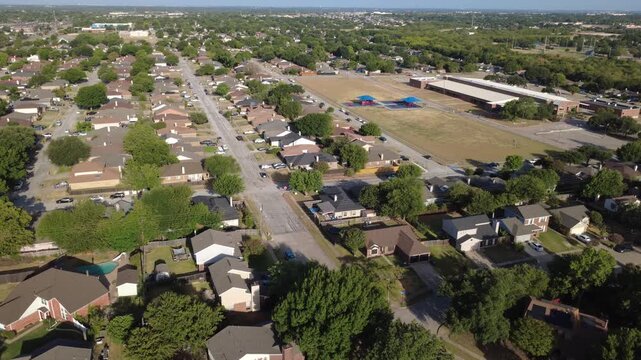 Spacious recreational sports fields border local elementary school near Charles City subdivision. Tidy suburban rooflines cluster around quiet paved roadways, foliage, Arlington, Texas