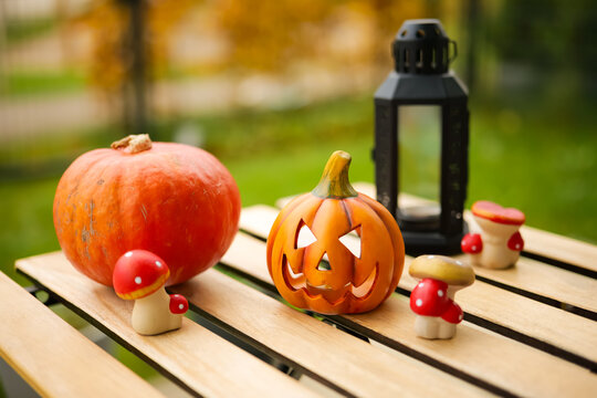 Autumn pumpkins and mushrooms with lantern displayed on wooden table outdoors.
