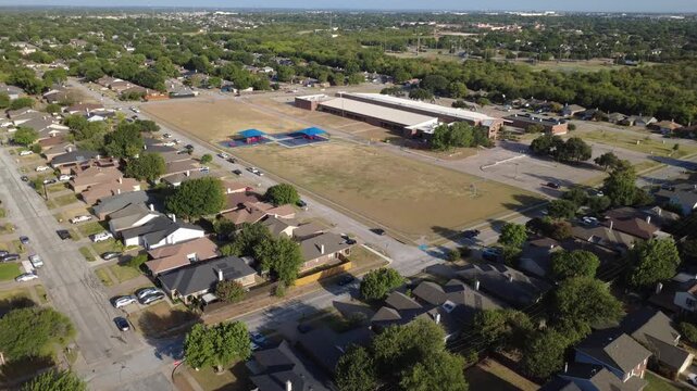 Wide open recreational grounds distinguish public elementary school campus near Charles City. Pitched shingle rooftops border expansive school property boundaries, lawns, Arlington, Texas