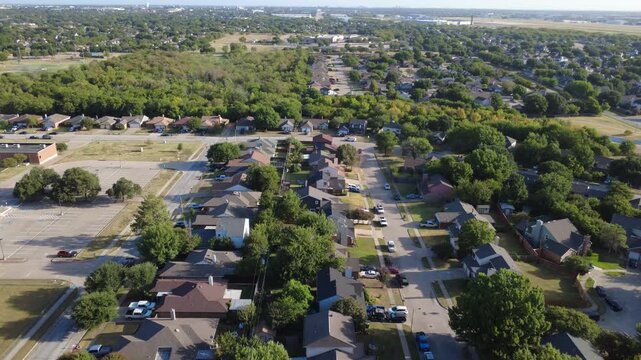 Orderly housing rows flank public elementary school grounds along Nicole Court subdivision. Paved parking lots border dense green forest preserves, residential avenues, Arlington, Texas