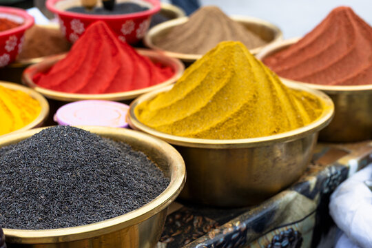Colorful spices in metal bowls at a traditional bazaar in Bukhara, Uzbekistan. Ground turmeric, paprika, and cumin seeds heaped in conical mounds create a vibrant market display ideal for travel.
