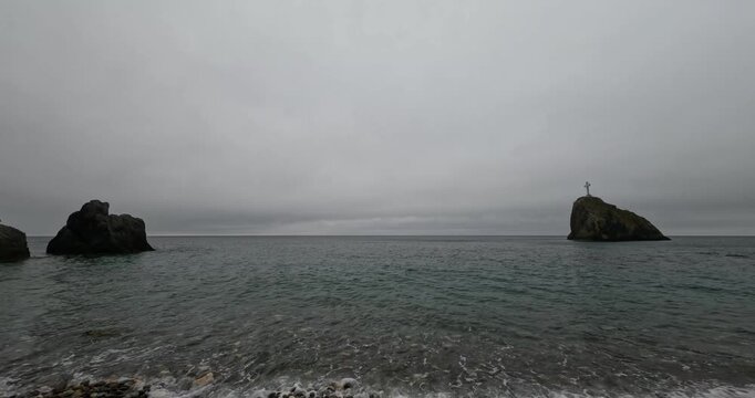 Religious cross monolith rises above coastal sea waters at Cape Fiolent under a dark gloomy sky. Static wide shot.