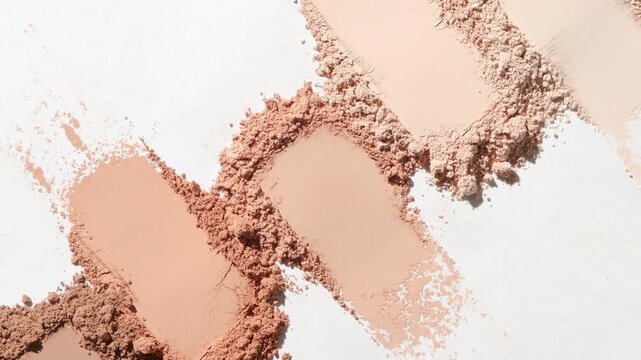 Top perspective extreme close-up of five beige aligned smears of loose powder on a white surface highlighted by moving light casting dynamic shadows