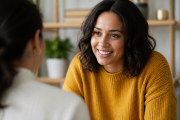 Obraz premium A smiling woman in a yellow sweater is talking to another person indoors.