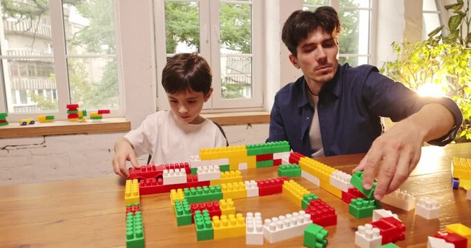 Father and son creating colorful brick layout while learning through play at home. Concept of STEM learning, family activity guides and construction toy ads.