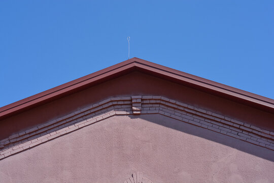 A building triangular gable roof with a single thin metal lightning rod wire mounted on the top ridge against a clear blue sky.