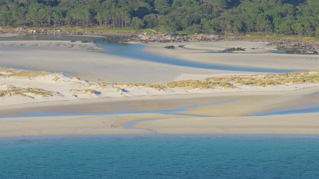 Aerial footage of Praia de Carnota, a scenic beach in Carnota, Galicia, Spain. The beach is partially populated, with people scattered along the shore, enjoying the natural landscape.