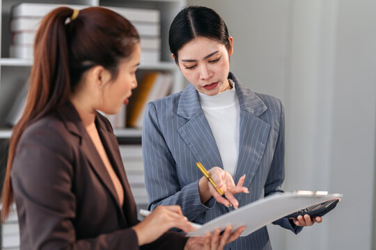 Asian Business Women Collaborate on Financial Report Using Calcu