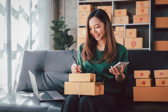 Asian Woman Managing Online Business Checking Orders on Phone Wr