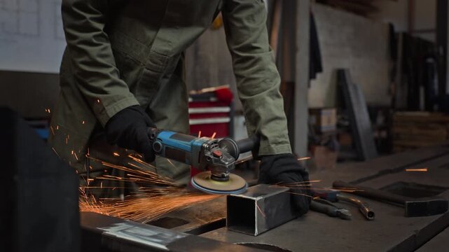 Caucasian male metalworker wearing protective face shield using angle grinder on steel pipe in workshop, camera tilting down. Footage is perfect for industrial manufacturing promotions