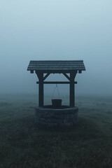 Naklejka premium Old water well in a misty meadow at dusk — part of a folk horror and dark poetry series 