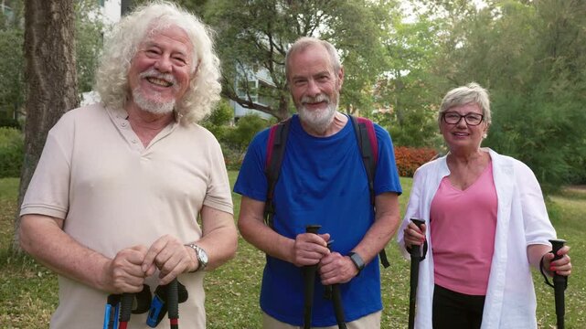 Three elderly friends with hiking poles smiling and laughing outdoors in a park