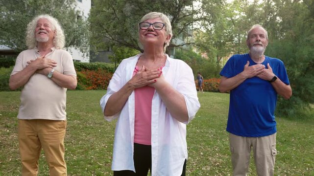 Three senior friends standing in a park with hands on their hearts, practicing gratitude