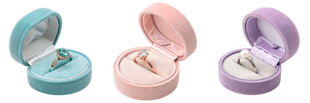 Three velvet ring boxes in different colors, each containing a ring, isolated on a white background.