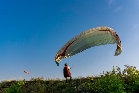 Person launching a paragliding wing on grassy hilltop