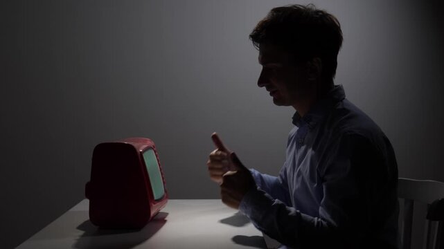 Man interacting with a retro television, giving a thumbs up gesture, signifying approval and positive reception to media content in a dimly lit setting