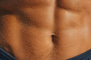 Fototapeta premium Tanned Male Torso with Water Drops and Sand at the Beach