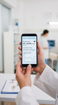 Doctor holding smartphone displays a health dashboard, empowering secure mobile banking for personal well-being and data-driven asset protection.
