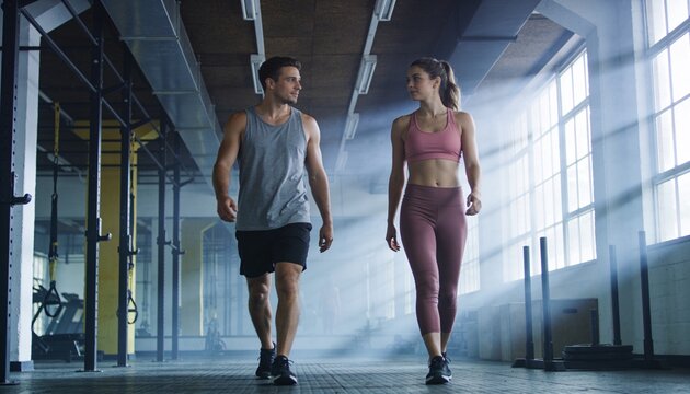 Walking man gray tank, woman pink sports bra down rubber floor, with rig and stacked plates
