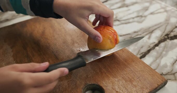 Kid hands cut with knife peach on wooden board. Boy prepare food in kitchen. 4K 10-bit