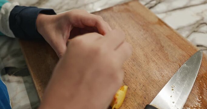 Kid hands cut with knife peach on wooden board. Boy prepare food in kitchen. 4K 10-bit