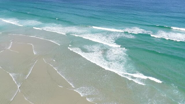 Aerial footage capturing the turquoise waves rolling onto the sandy shore of Praia do Rostro, located on the Atlantic coast of Spain.