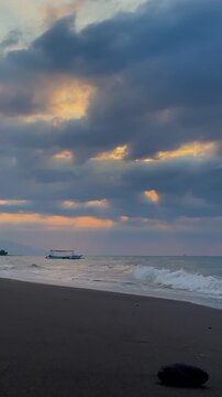 Vertical shot Traditional boat floating on calm sea during moody sunset in Bali
