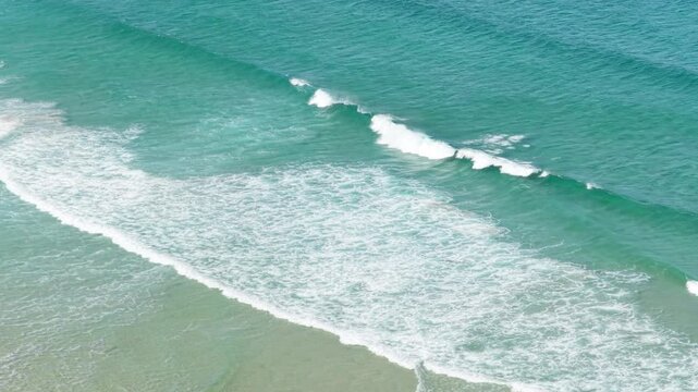 Aerial view of turquoise ocean waves gently rolling onto the sandy shore at Praia do Rostro, located on the coast of Spain.
