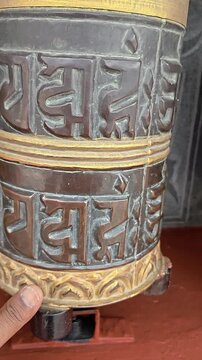 Vertical footage of a traditional Buddhist prayer wheel decorated with the sacred Om Mani Padme Hum mantra and ornamental Buddhist artwork. The close-up captures the detailed religious craftsmanship